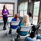 A woman stands before a group, confidently presenting her topic and interacting with the audience during the session.
