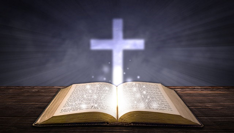 An open Bible sits on a wooden table, with a cross placed behind it, symbolizing faith and spirituality.
